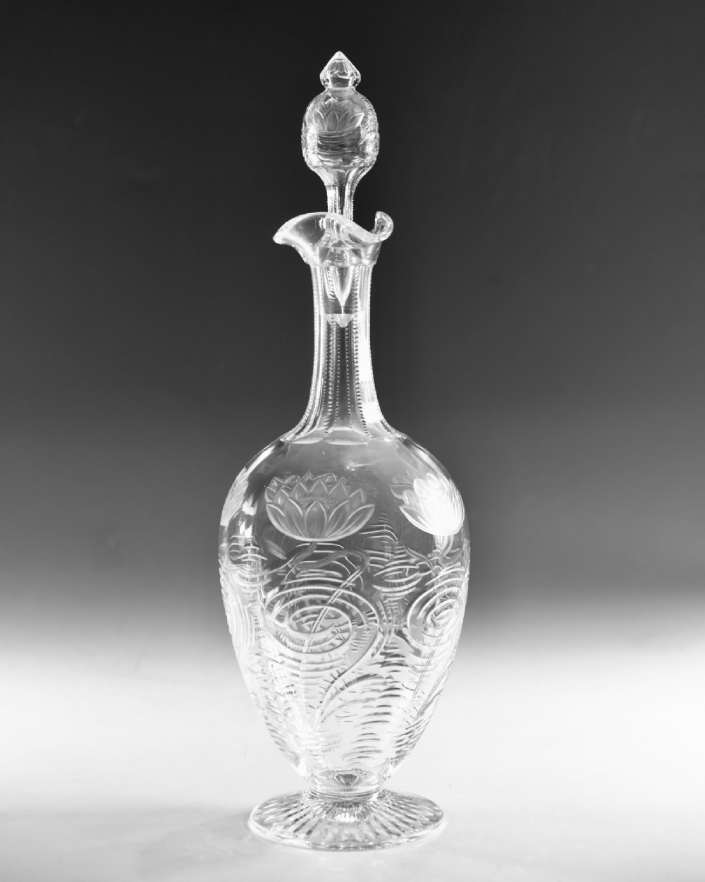 A pair of antique clear glass decanters with intaglio water lily engravings, tall slender necks, and matching glass stoppers. View III