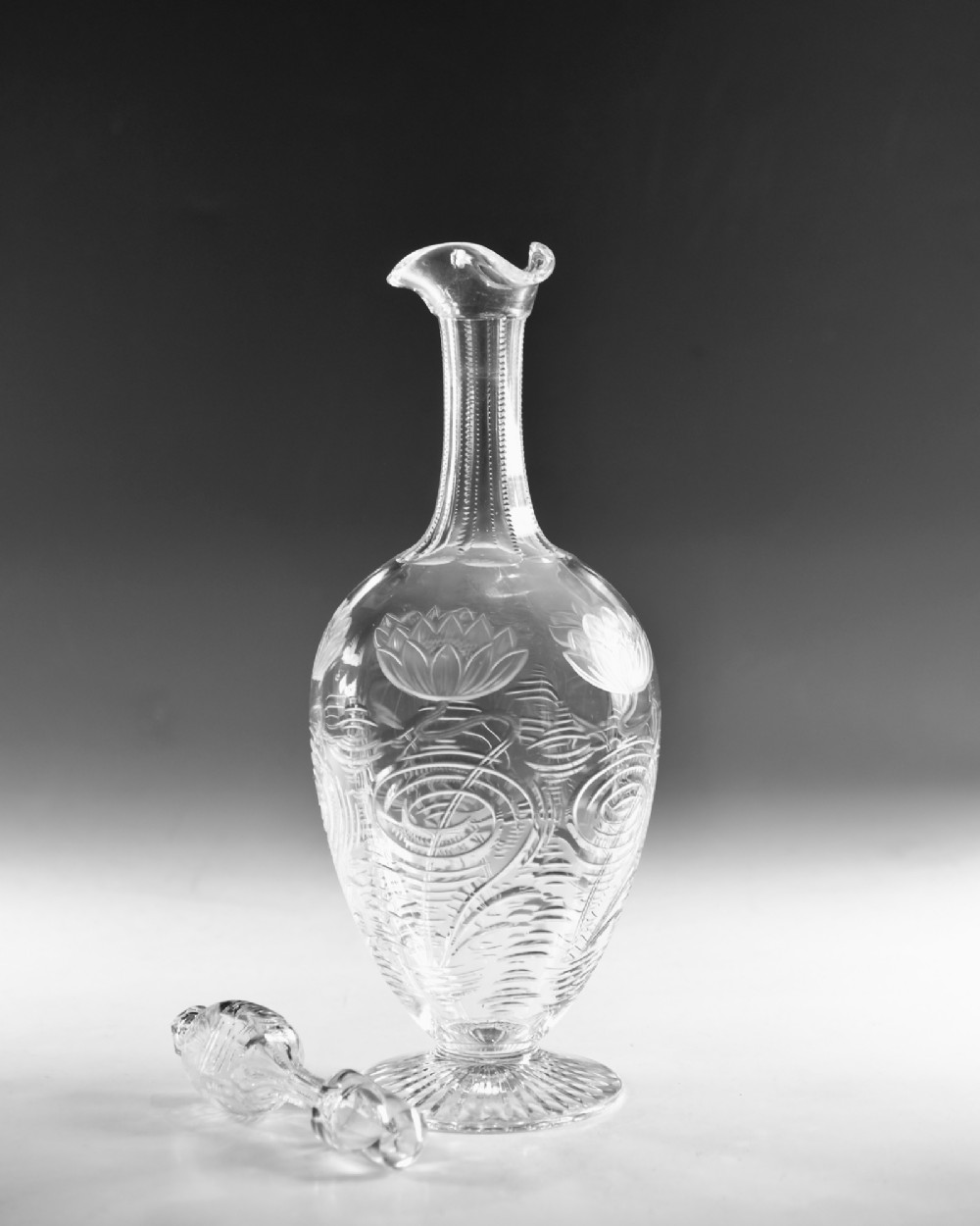 A pair of antique clear glass decanters with intaglio water lily engravings, tall slender necks, and matching glass stoppers. View IV