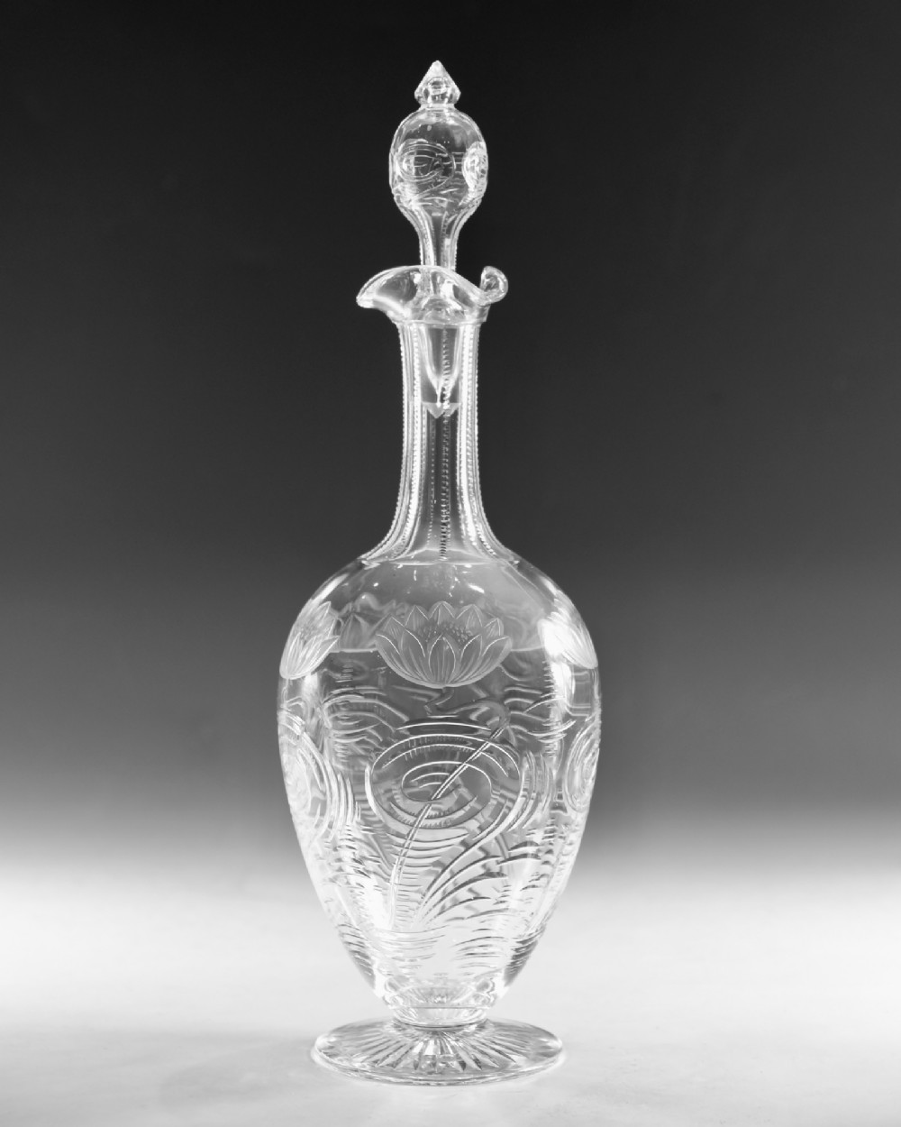 A pair of antique clear glass decanters with intaglio water lily engravings, tall slender necks, and matching glass stoppers. View VIII