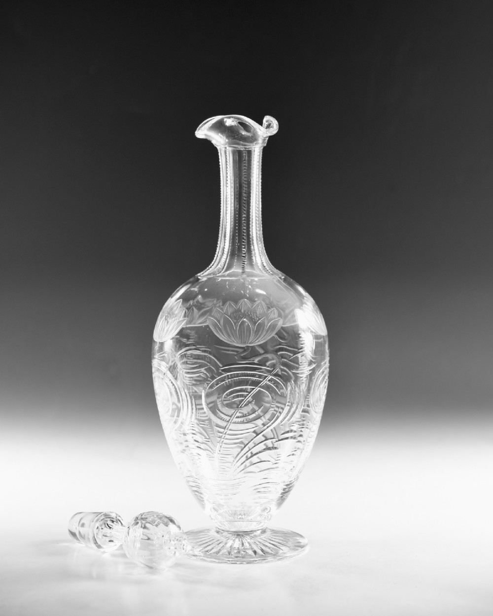 A pair of antique clear glass decanters with intaglio water lily engravings, tall slender necks, and matching glass stoppers. View IX