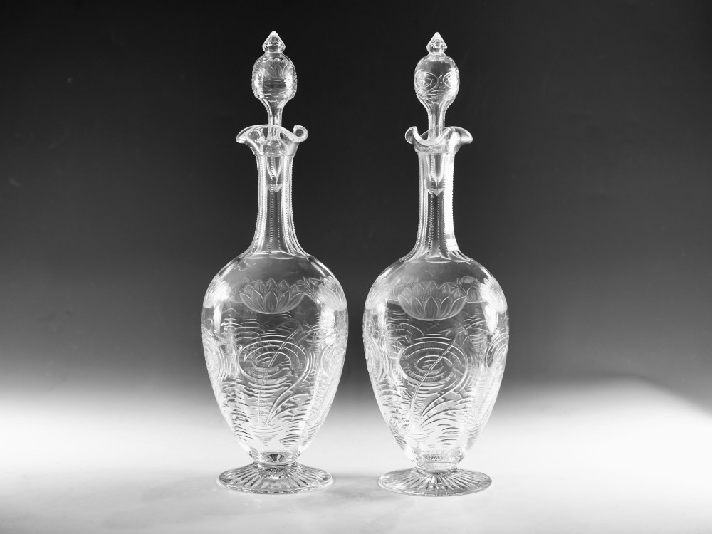 A pair of antique clear glass decanters with intaglio water lily engravings, tall slender necks, and matching glass stoppers. View XIII