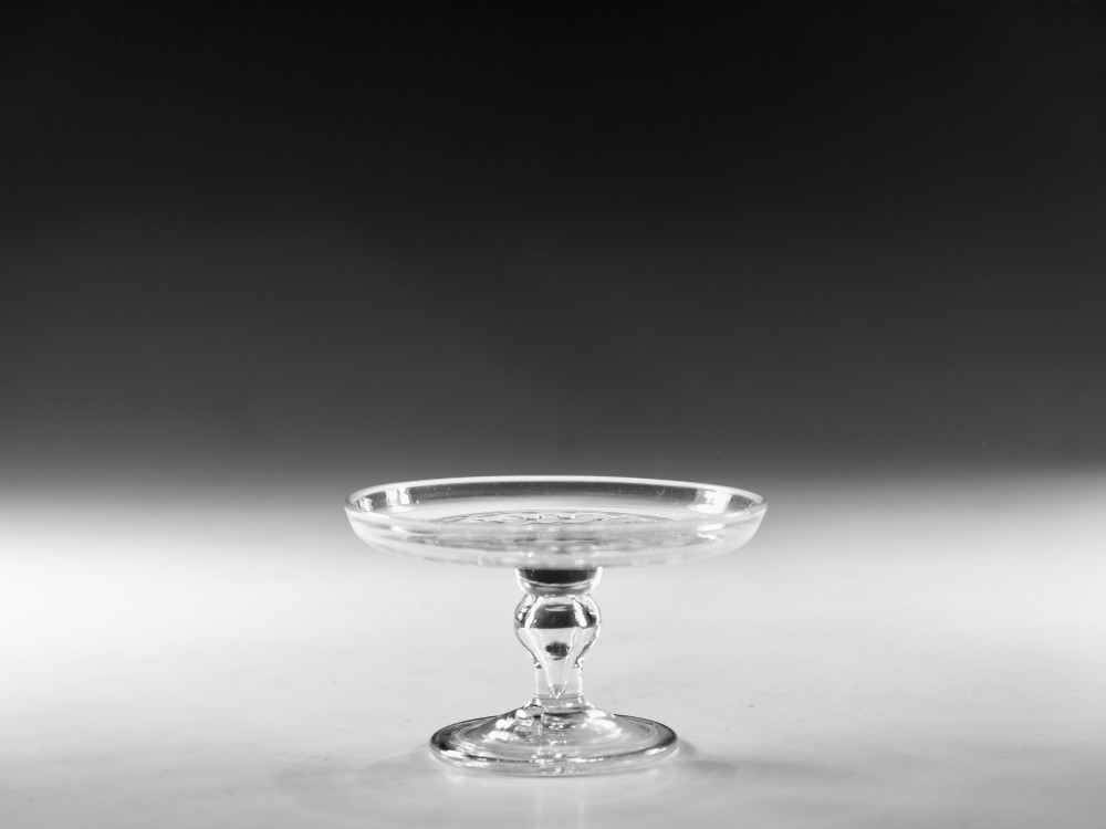A clear Georgian lead glass patch stand featuring a shallow circular top dish elevated on a baluster stem and a spreading foot.