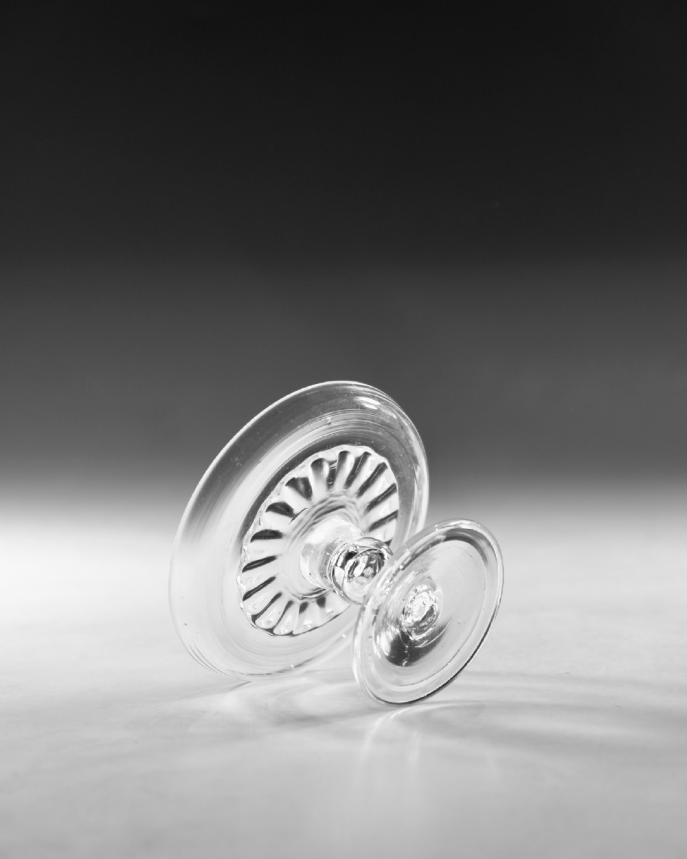 A clear Georgian lead glass patch stand featuring a shallow circular top dish elevated on a baluster stem and a spreading foot. View V