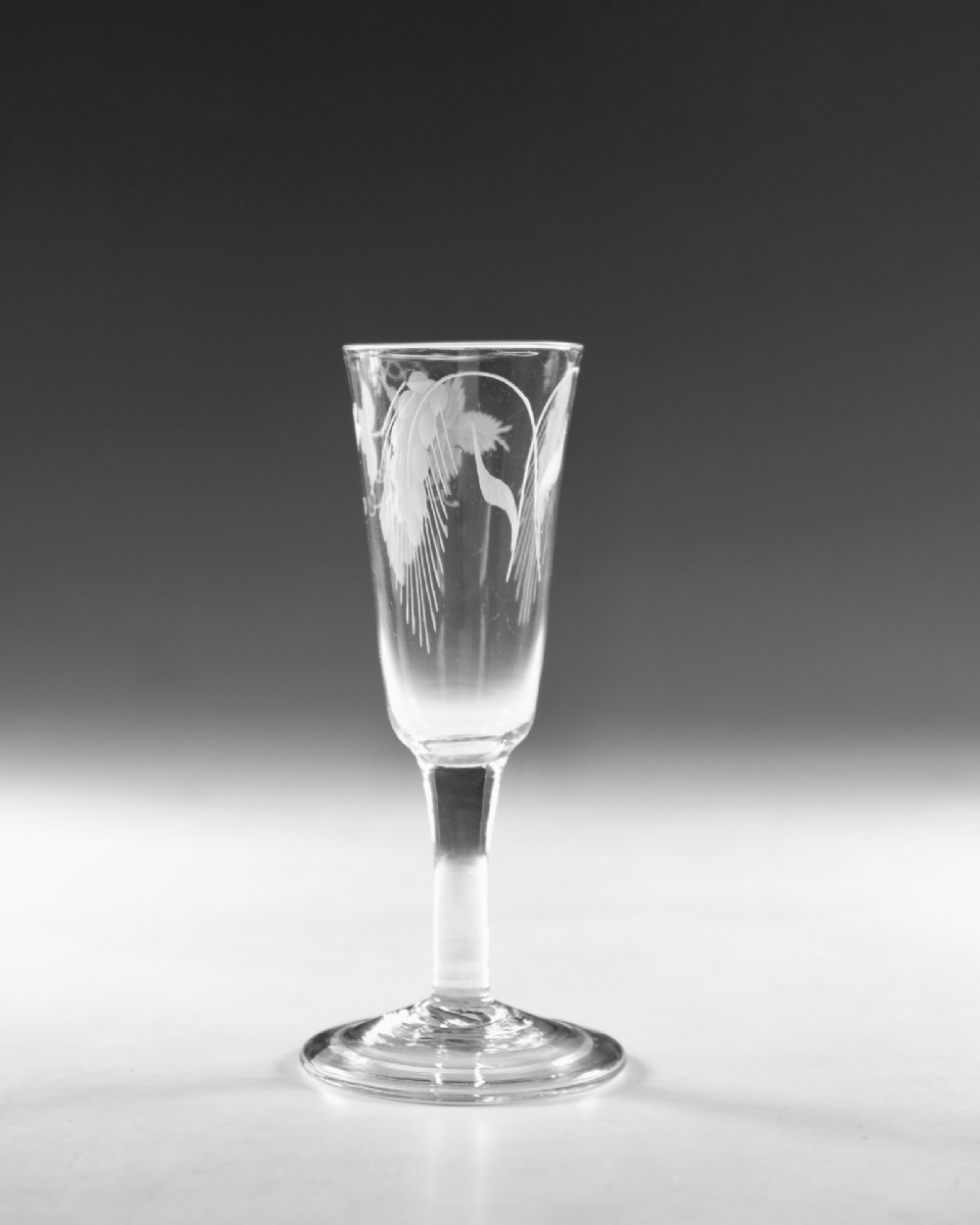 A tall Georgian clear glass ale flute with an engraved hop and barley motif, a straight plain stem, and a flat conical base. View III