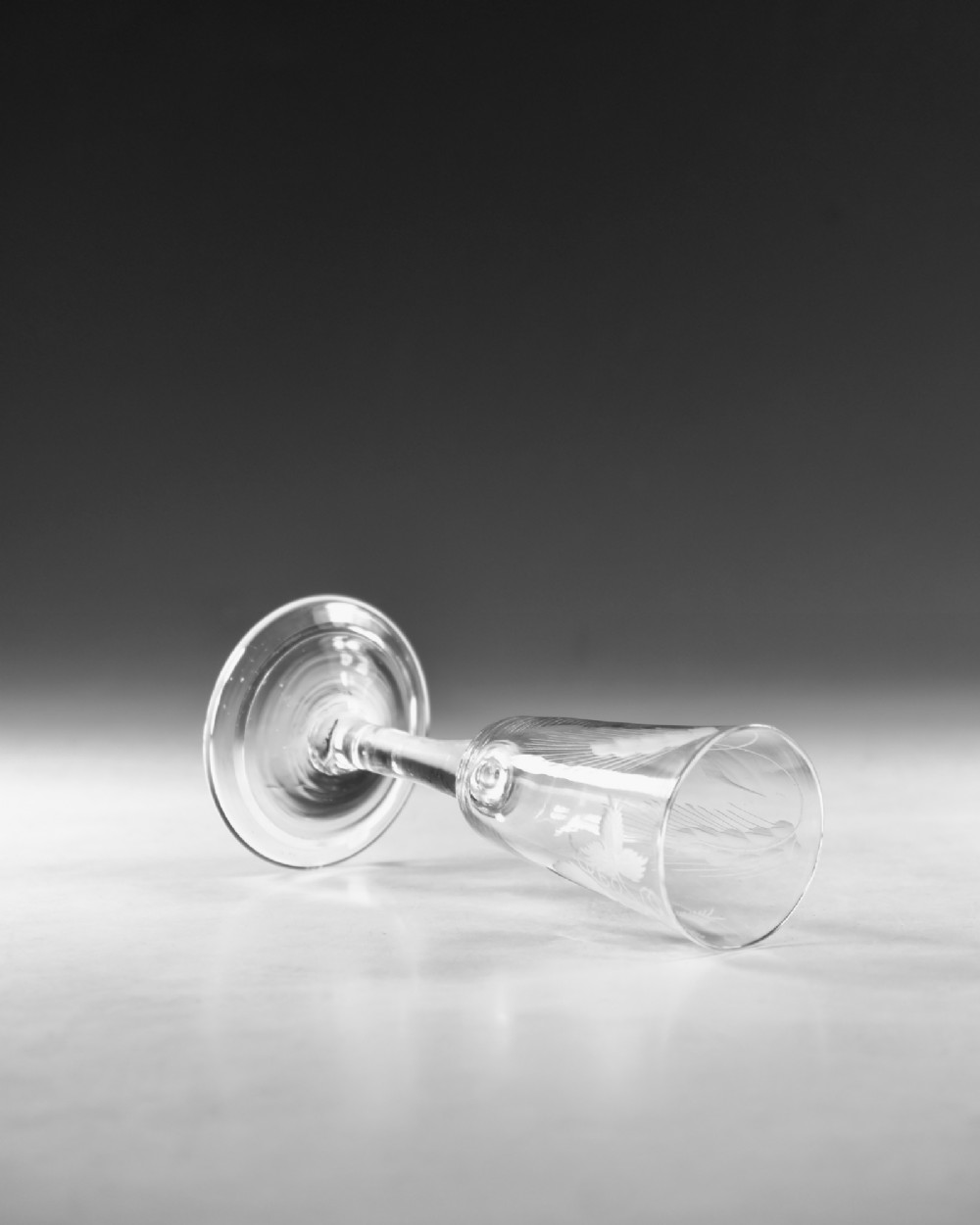 A tall Georgian clear glass ale flute with an engraved hop and barley motif, a straight plain stem, and a flat conical base. View V