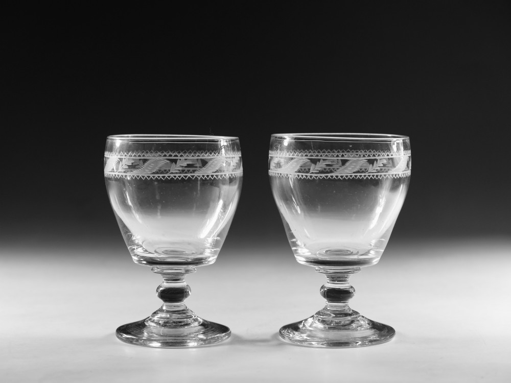 A pair of clear Georgian glass rummers with hand-engraved geometric borders and knopped stems on circular bases.