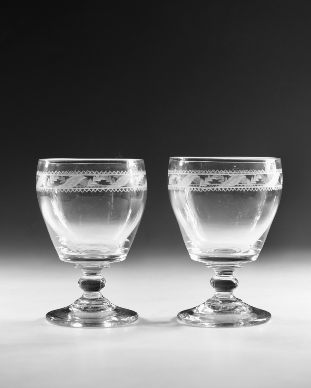 A pair of clear Georgian glass rummers with hand-engraved geometric borders and knopped stems on circular bases. View II