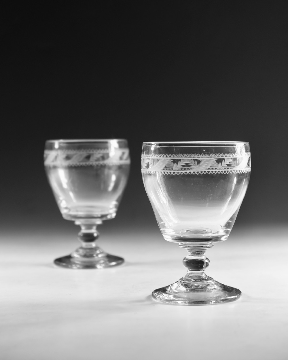 A pair of clear Georgian glass rummers with hand-engraved geometric borders and knopped stems on circular bases. View IV