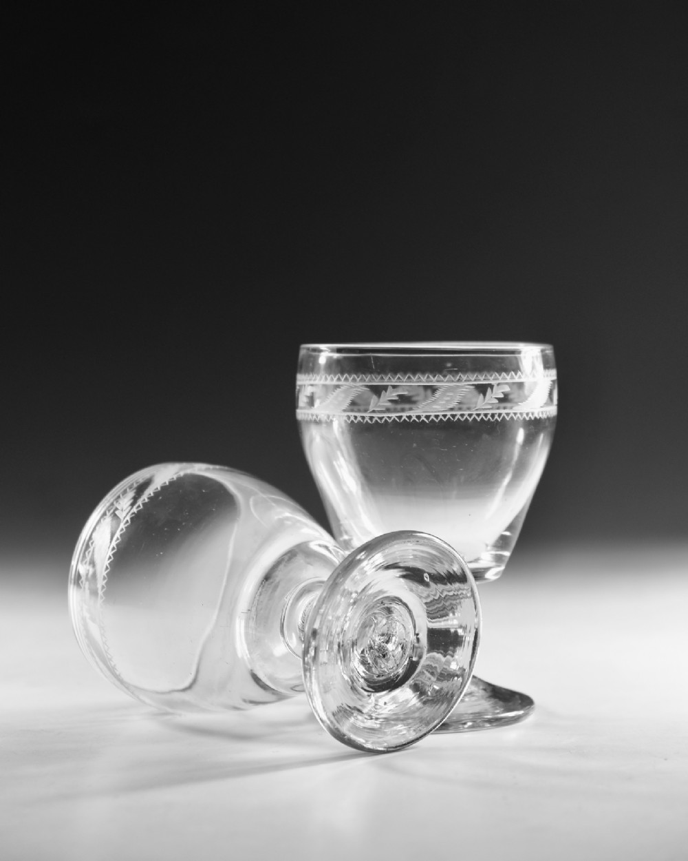 A pair of clear Georgian glass rummers with hand-engraved geometric borders and knopped stems on circular bases. View V