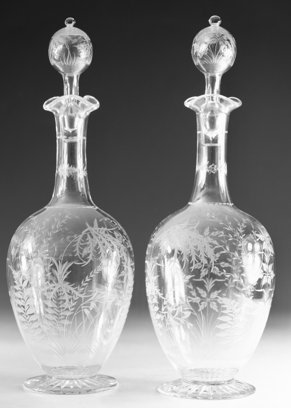 A pair of clear Victorian glass decanters featuring etched botanical fern decoration, narrow necks, ruffled collars, and spherical stoppers. View II