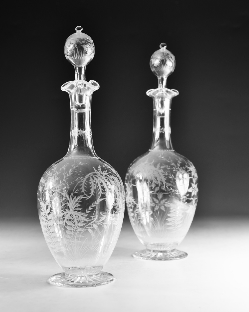 A pair of clear Victorian glass decanters featuring etched botanical fern decoration, narrow necks, ruffled collars, and spherical stoppers. View III