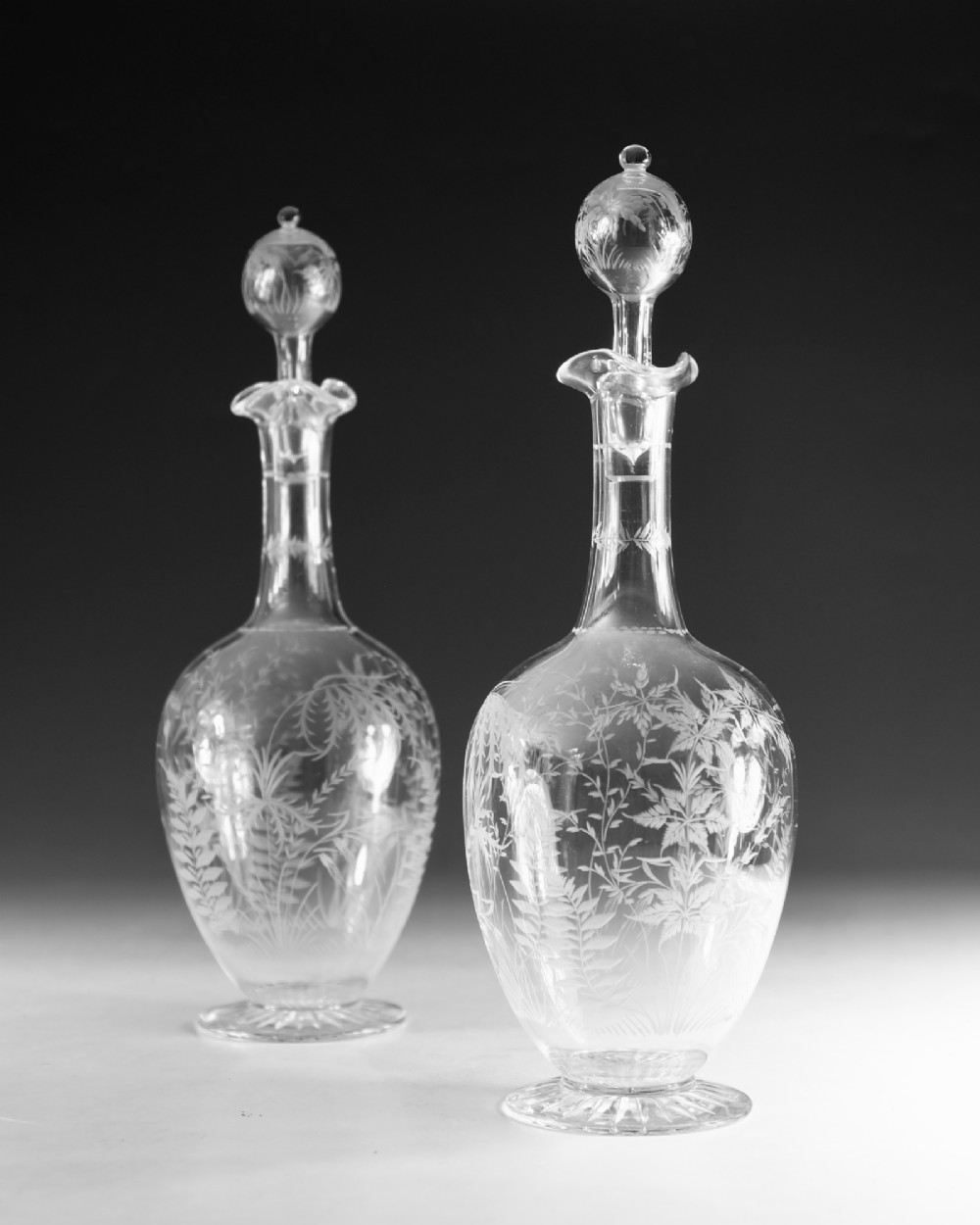 A pair of clear Victorian glass decanters featuring etched botanical fern decoration, narrow necks, ruffled collars, and spherical stoppers. View IV