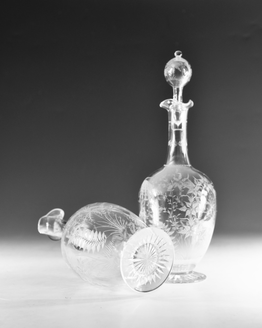 A pair of clear Victorian glass decanters featuring etched botanical fern decoration, narrow necks, ruffled collars, and spherical stoppers. View V