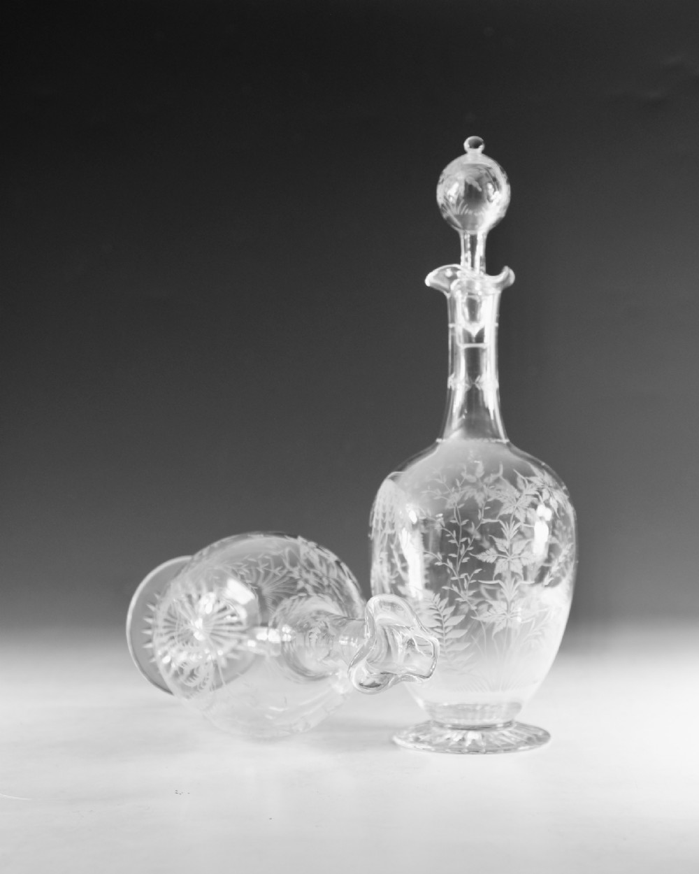 A pair of clear Victorian glass decanters featuring etched botanical fern decoration, narrow necks, ruffled collars, and spherical stoppers. View VI