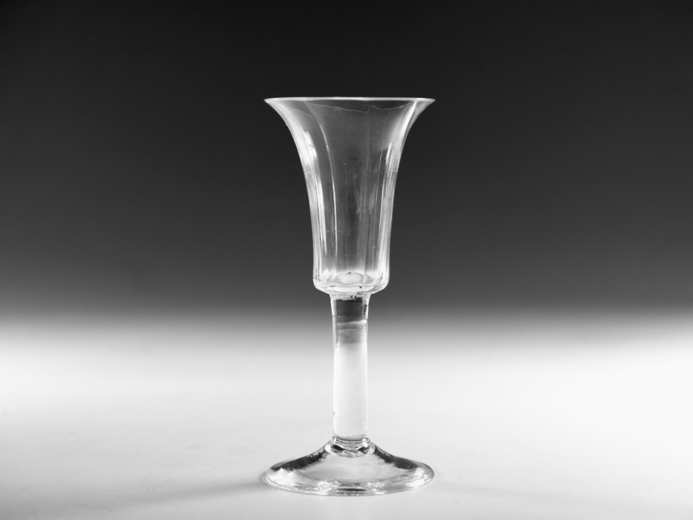 An eighteenth-century clear lead glass ale flute featuring a ribbed trumpet-shaped bowl on a straight stem with a conical base.