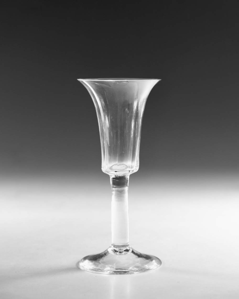 An eighteenth-century clear lead glass ale flute featuring a ribbed trumpet-shaped bowl on a straight stem with a conical base. View II