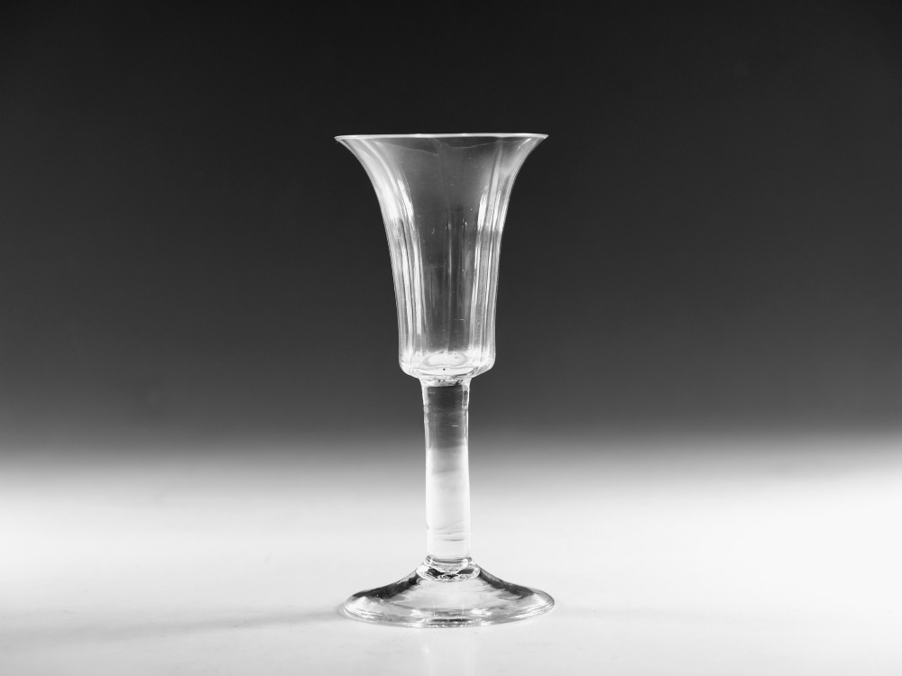An eighteenth-century clear lead glass ale flute featuring a ribbed trumpet-shaped bowl on a straight stem with a conical base. View VI