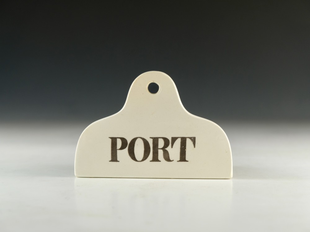 A mid-19th century creamware ceramic bin label with a top hole and the word PORT printed in bold black lettering.