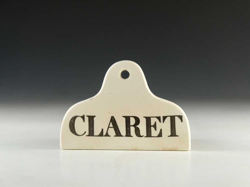 A mid 19th-century cream ceramic wine bin label stamped with the word CLARET in black serif lettering.