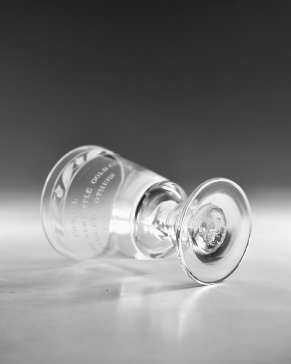An antique clear glass Georgian rummer featuring wheel-engraved inscriptions and foliage motifs above a knopped stem. View V