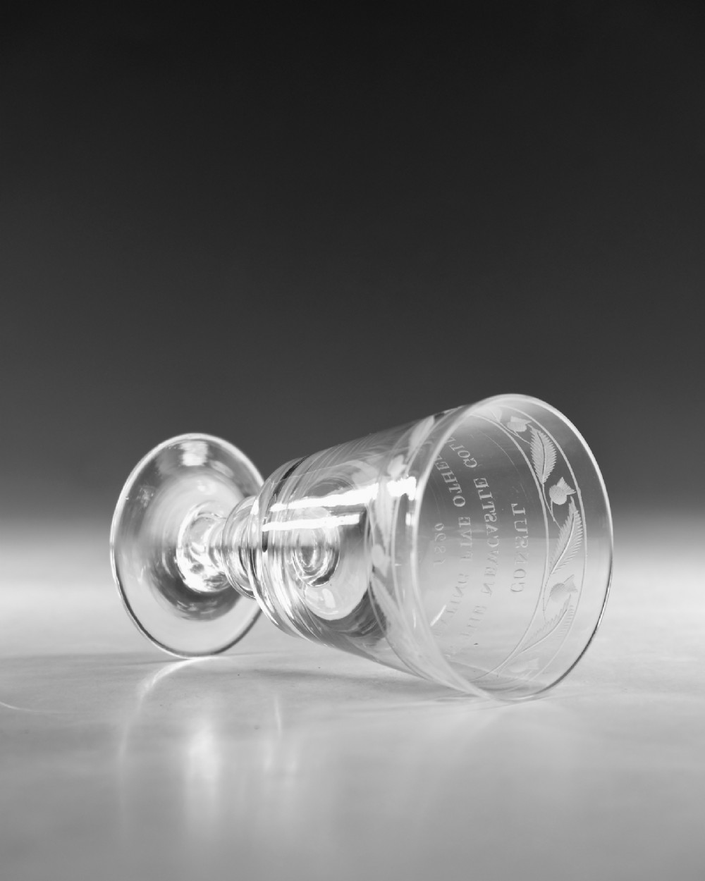 An antique clear glass Georgian rummer featuring wheel-engraved inscriptions and foliage motifs above a knopped stem. View VI
