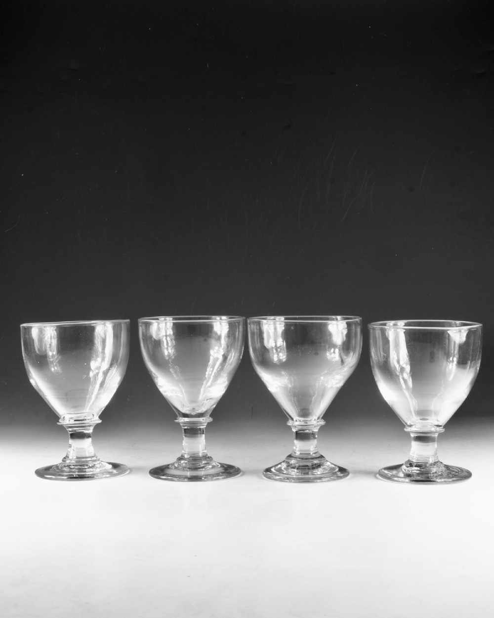 A set of four clear hand-blown Georgian glass rummers with wide funnel bowls, short collar stems, and circular flat bases. View II