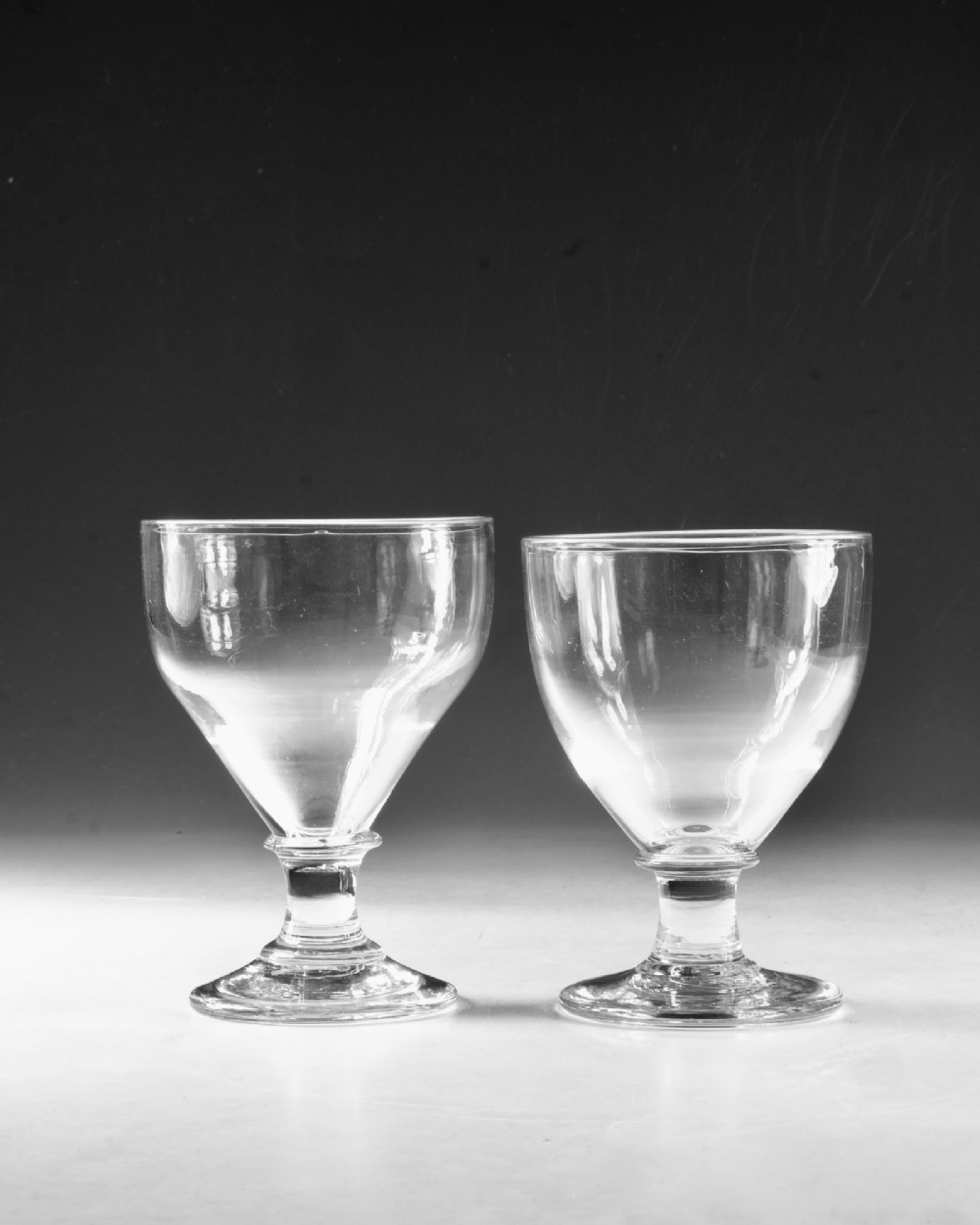 A set of four clear hand-blown Georgian glass rummers with wide funnel bowls, short collar stems, and circular flat bases. View V