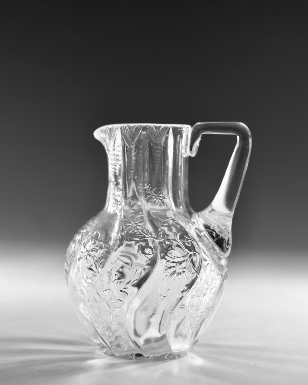 An antique clear glass jug featuring a bulbous swirl-moulded lower body with wheel-engraved floral motifs and a fitted handle. View II