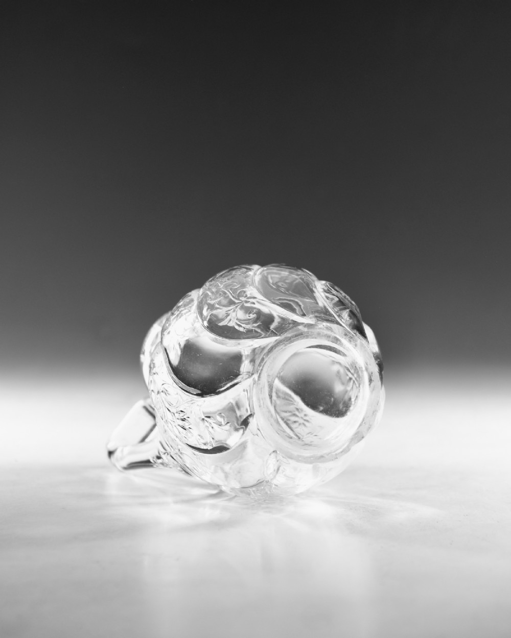 An antique clear glass jug featuring a bulbous swirl-moulded lower body with wheel-engraved floral motifs and a fitted handle. View VII
