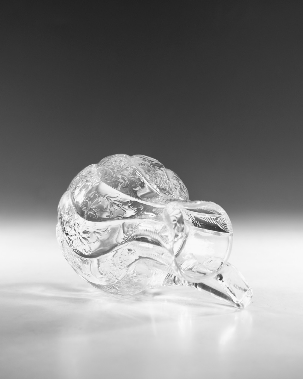 An antique clear glass jug featuring a bulbous swirl-moulded lower body with wheel-engraved floral motifs and a fitted handle. View IX