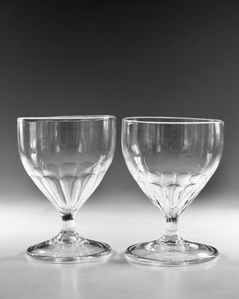 A pair of antique Georgian clear glass rummers featuring wide cylindrical bowls with fluted lower panels on short stems and circular bases. View II