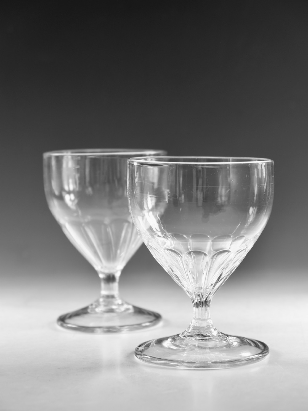 A pair of antique Georgian clear glass rummers featuring wide cylindrical bowls with fluted lower panels on short stems and circular bases. View V