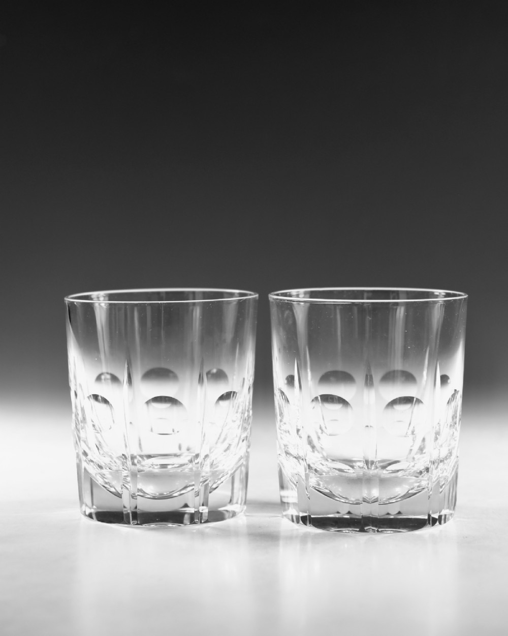 A pair of early twentieth-century clear cut glass tumblers featuring circular lens cuts and vertical fluting. View II