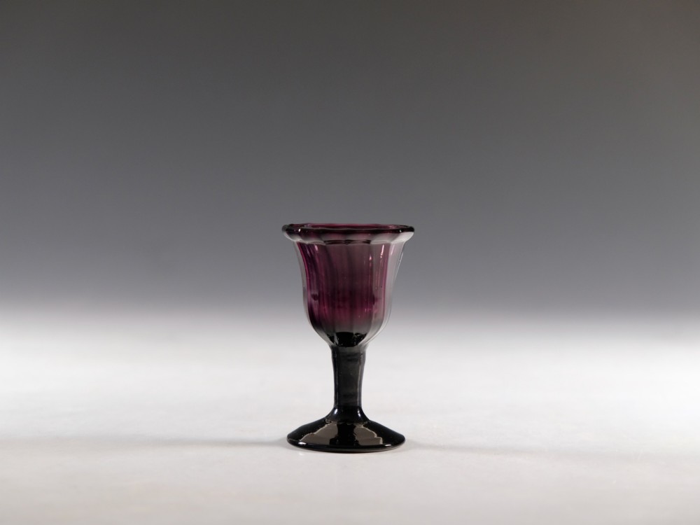 A Georgian amethyst purple glass egg cup with a fluted bowl, slender stem, and circular pedestal foot.