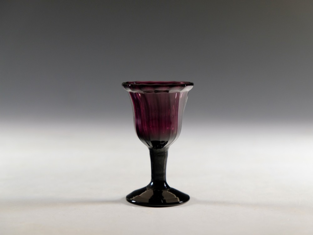 A Georgian amethyst purple glass egg cup with a fluted bowl, slender stem, and circular pedestal foot. View VI