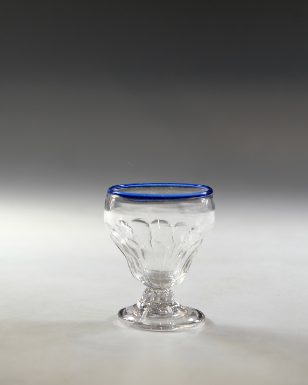 An 18th-century clear lead glass bonnet glass featuring a hand-applied cobalt blue rim, a honeycomb-moulded cup bowl, and a circular flat foot.