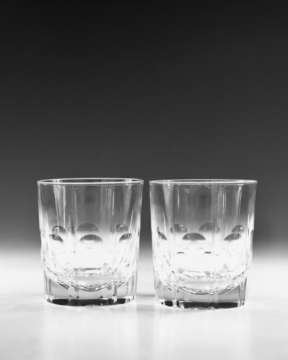 A pair of early 20th-century clear cut crystal tumblers featuring circular lens cuts and vertical faceted detail around the lower half. View II
