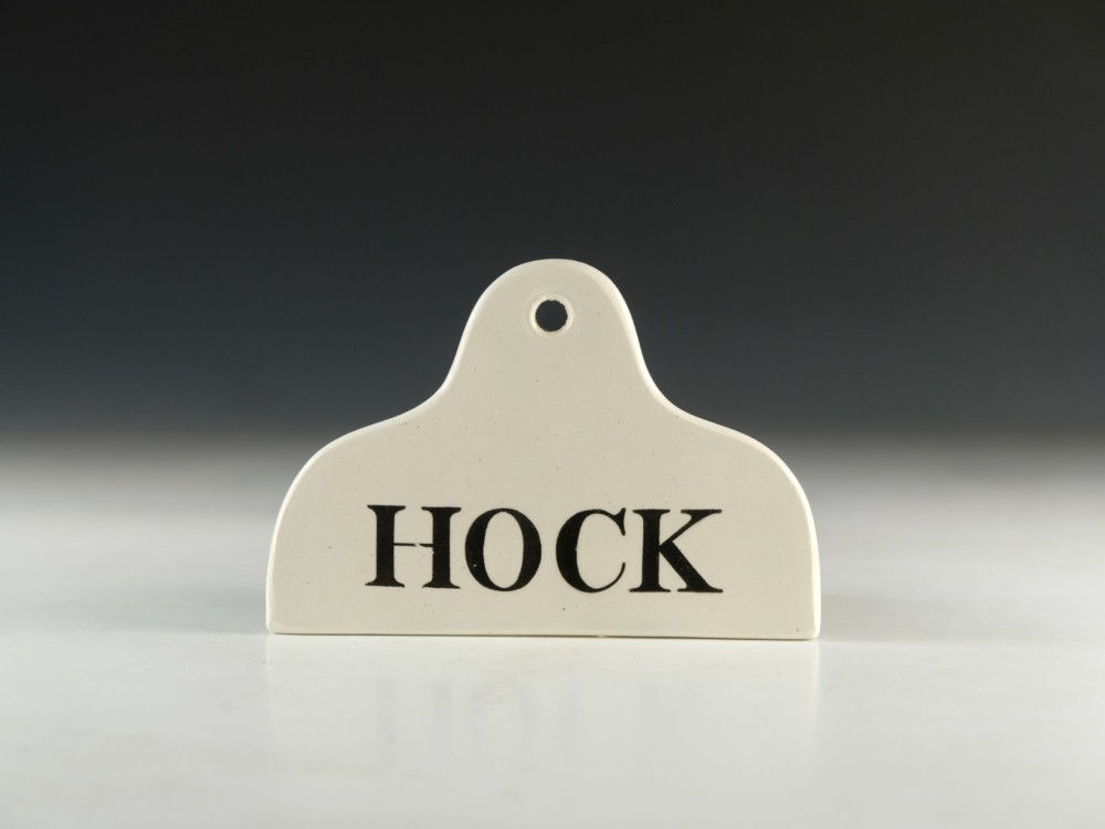 A cream glazed ceramic wine bin label with an arched top, single hanging hole, and black printed serif text reading HOCK.