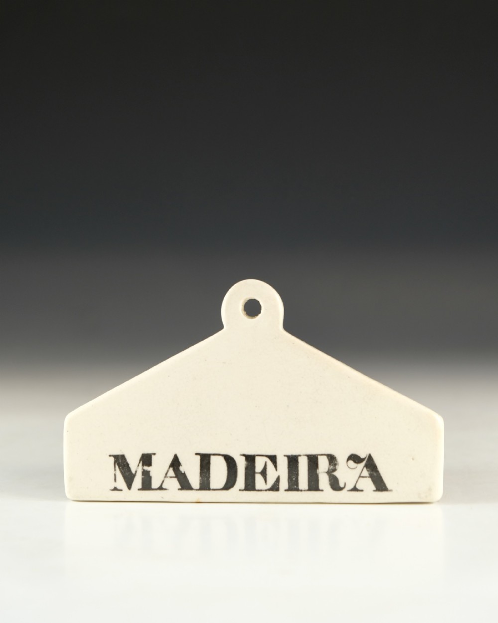 A mid-19th-century white ceramic wine bin label with a top mounting hole, printed with the text MADEIRA in black capital letters.