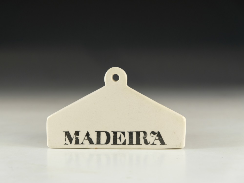 A mid-19th-century white ceramic wine bin label with a top mounting hole, printed with the text MADEIRA in black capital letters. View II