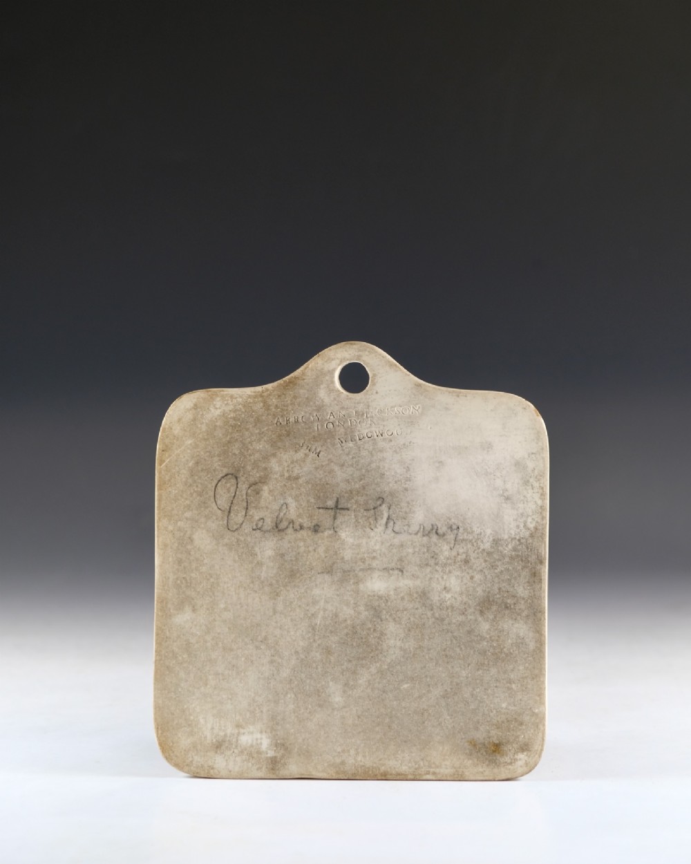 An off-white ceramic wine cellar bin label featuring an arched top with a central hanging hole, impressed maker marks, and cursive writing reading Velvet Sherry. View II