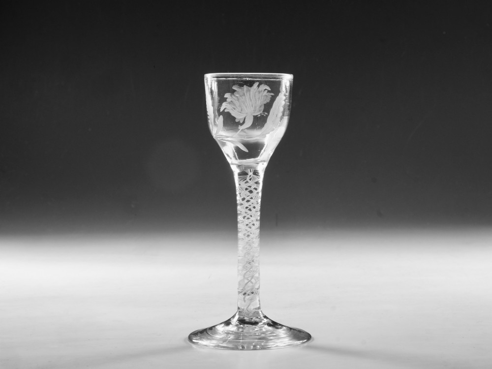 An 18th-century Georgian clear glass wine goblet featuring a wheel-engraved floral bowl, an internal opaque white twist stem, and a flat conical base.