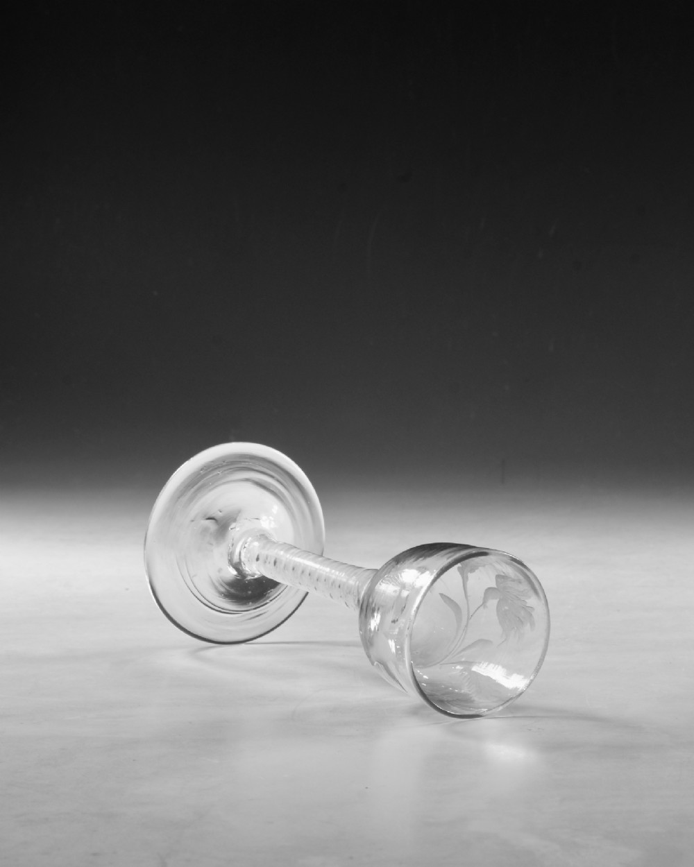 An 18th-century Georgian clear glass wine goblet featuring a wheel-engraved floral bowl, an internal opaque white twist stem, and a flat conical base. View V