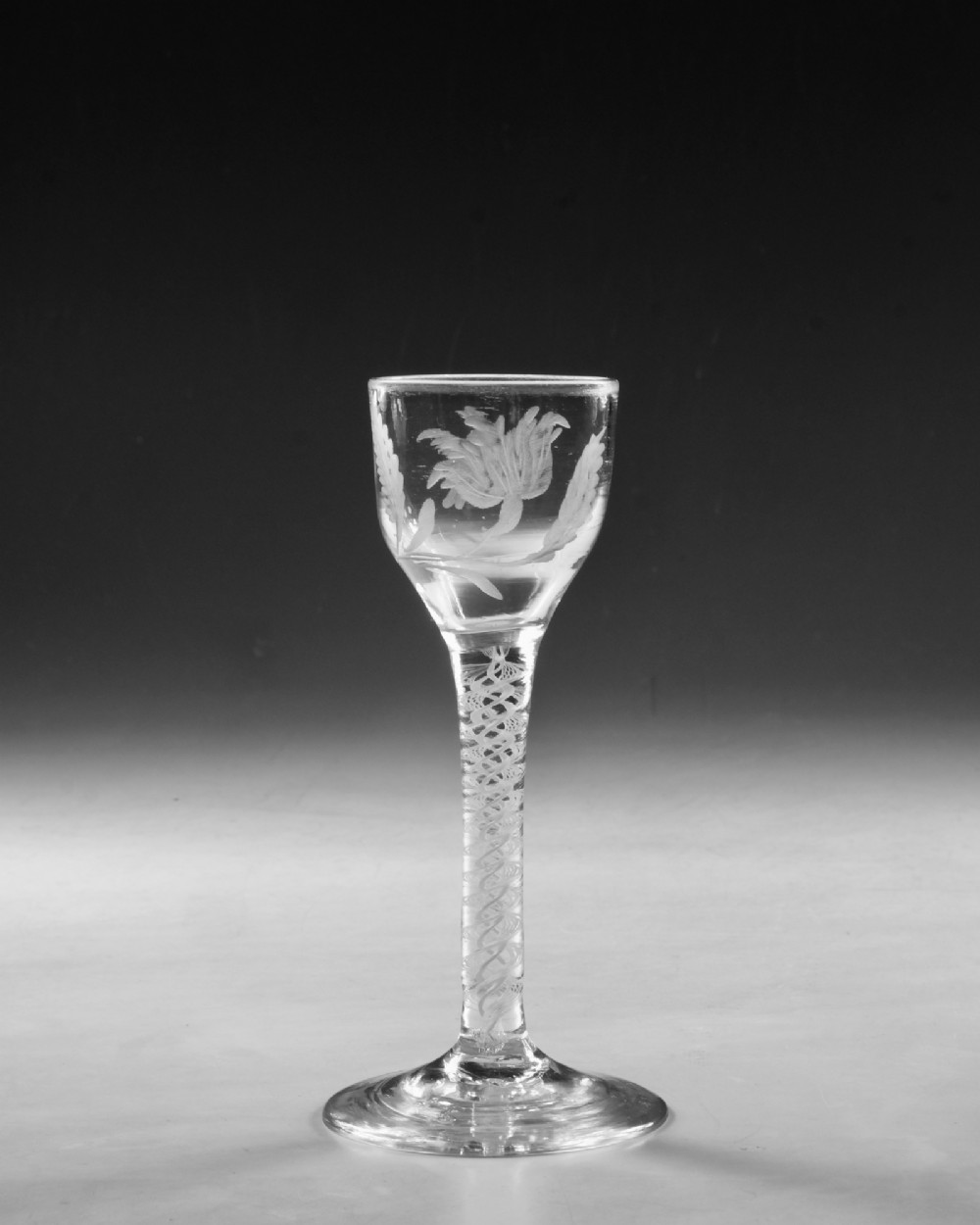 An 18th-century Georgian clear glass wine goblet featuring a wheel-engraved floral bowl, an internal opaque white twist stem, and a flat conical base. View VII