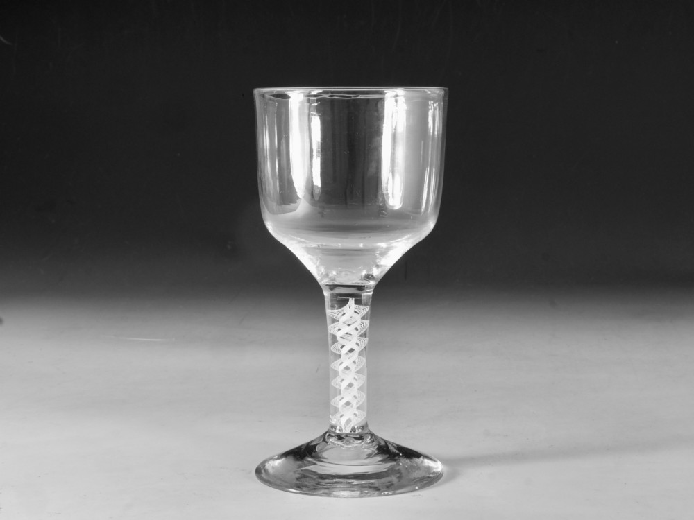 An 18th-century clear glass wine goblet featuring a round bowl supported by an opaque white spiral twist stem on a conical foot.