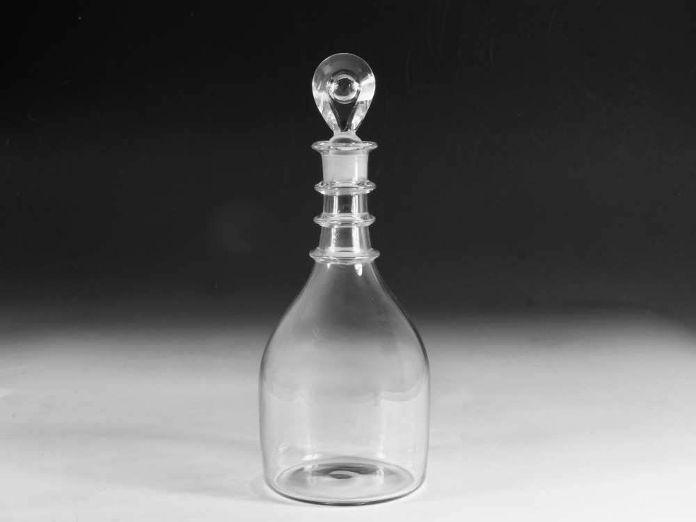 A clear Georgian glass decanter featuring three applied neck rings and a flat circular stopper.