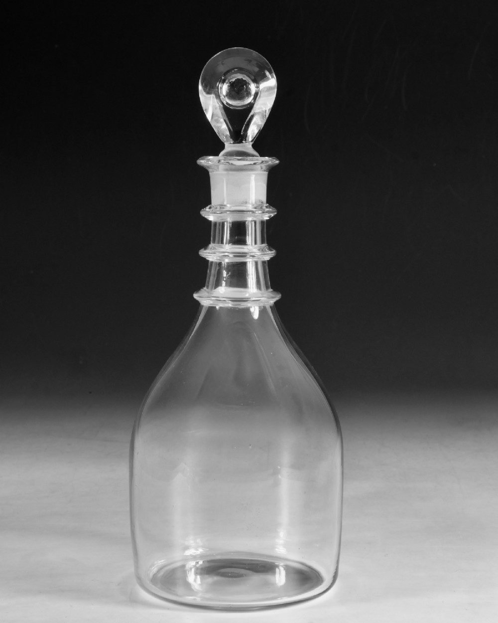 A clear Georgian glass decanter featuring three applied neck rings and a flat circular stopper. View II