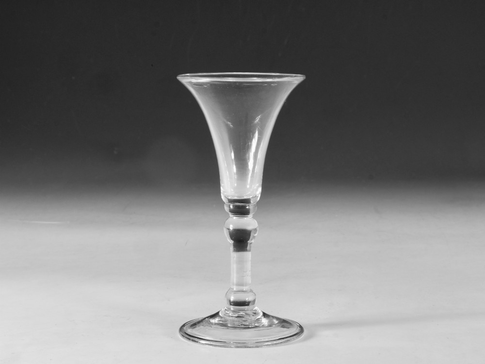 A mid-18th century clear Georgian glass featuring a flared trumpet bowl, a knopped stem, and a broad circular foot.