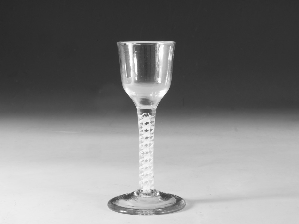 A clear Georgian lead glass wine glass featuring a tall bowl, an intricate white opaque twist stem, and a circular flat foot.