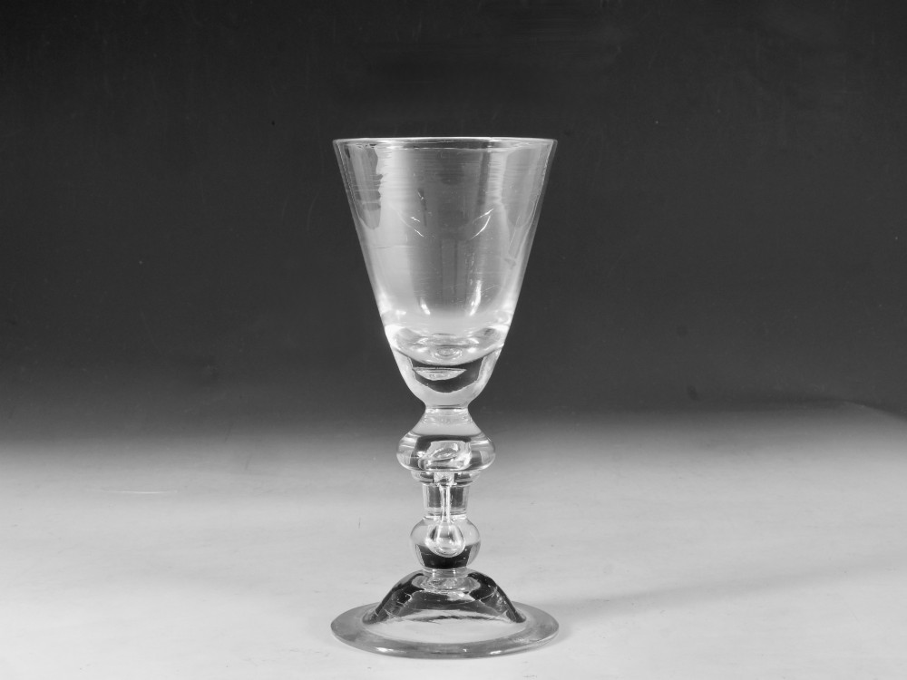 A hand-blown clear lead glass baluster wine goblet featuring a bell bowl, knopped stem with an air tear inclusion, and a folded conical foot.